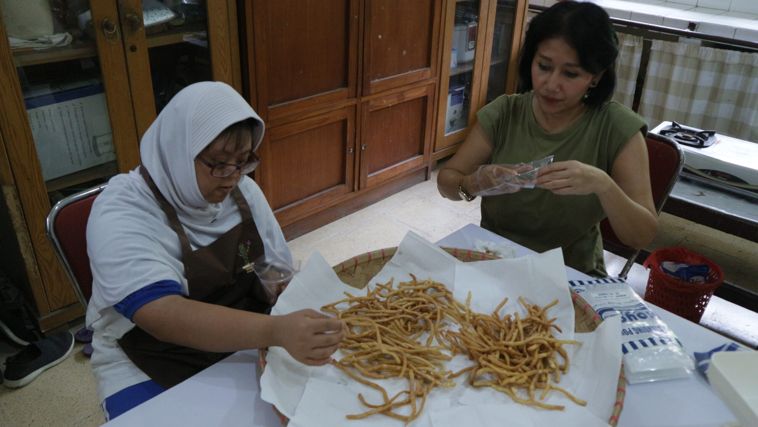 Saphira dan Bu Devi, salah seorang orang tua murid dari kelas SDLB Ulaka Penca membantu pengemasan snack cheese stick sebelum dijual, (dok.pribadi/Iglo Montana).